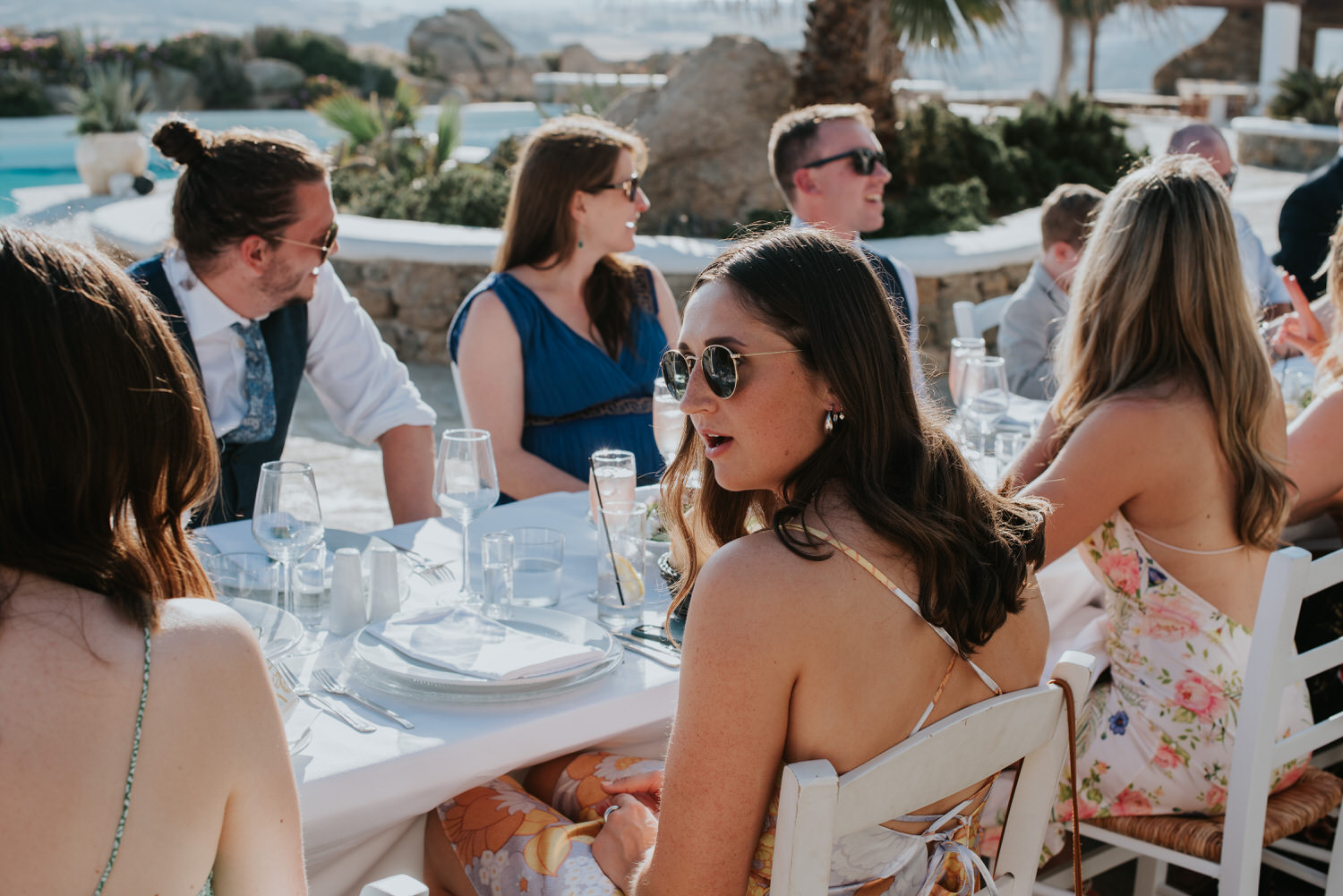 Mykonos wedding photographer: guests sat chatting at the reception table basked in the sun.