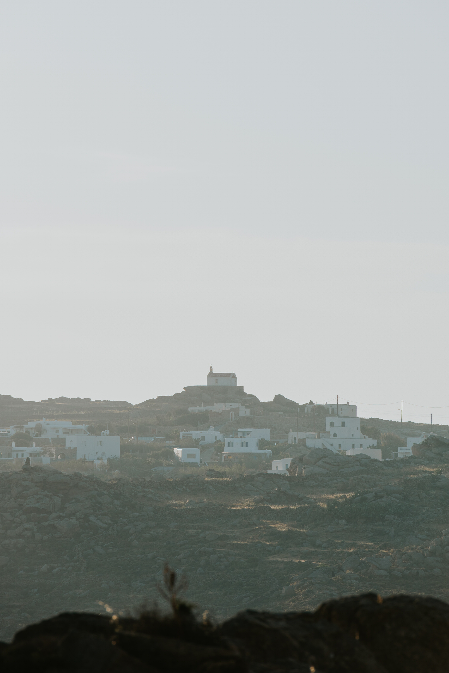 Mykonos wedding photographer: red roof church in sunset light on the hill top in Mykonian landscape.