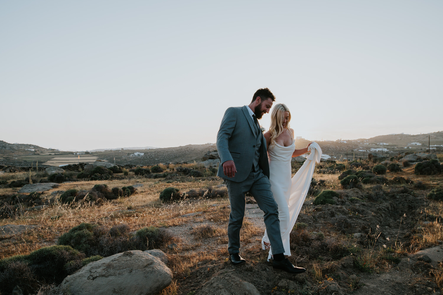Mykonos wedding photographer: bride and groom having fun walking in sunset light through grassy field.