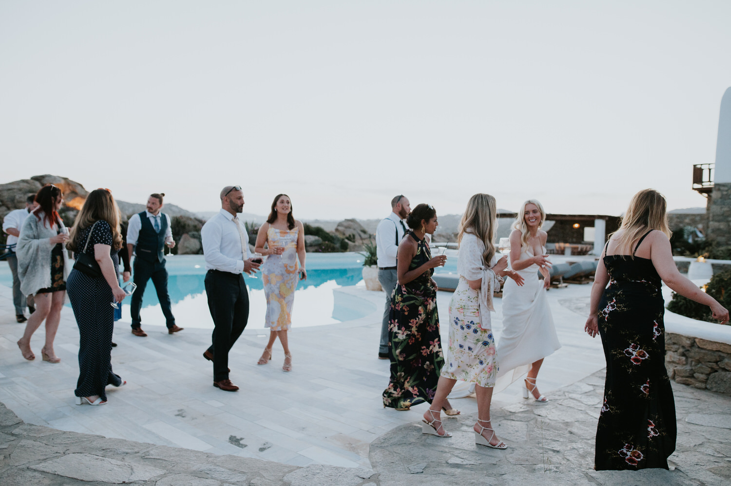 Mykonos wedding photographer: wedding guests walking pass the turquoise swimming pall on Mykonos wedding at a villa.