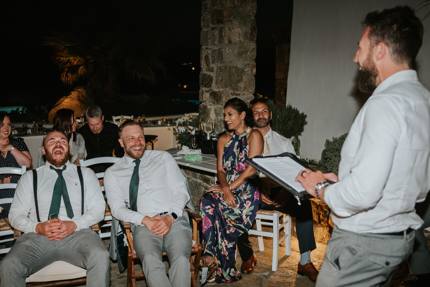 Mykonos wedding photographer: groom and his best men laughing surrounded by guests during his speeches on Mykonos wedding.
