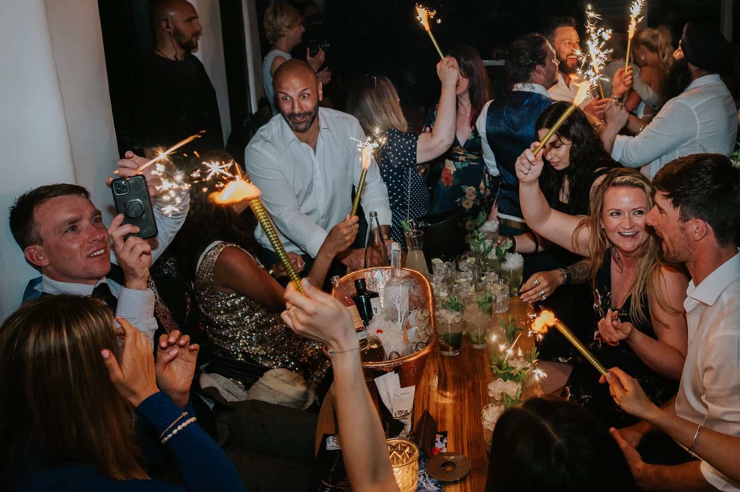 Mykonos wedding photographer: guests all having fun with sparklers at their table at Scarpa bar for Mykonos wedding celebration.