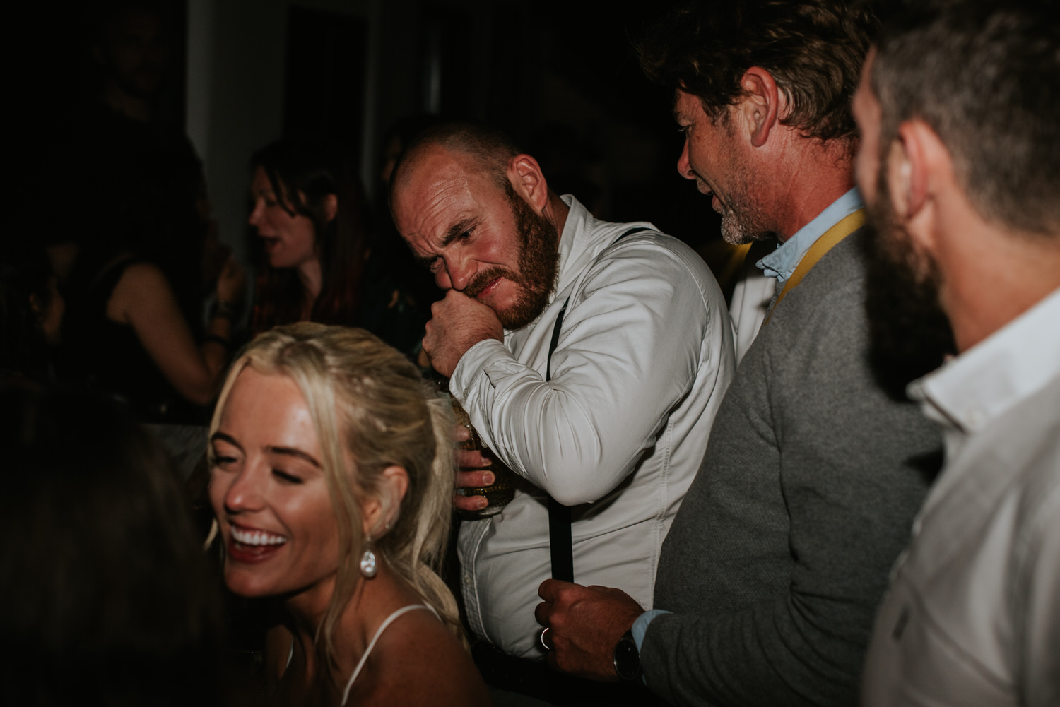Mykonos wedding photographer: wedding guest skilfully opening a bottle with his teeth on the dance floor for Mykonos wedding celebration.