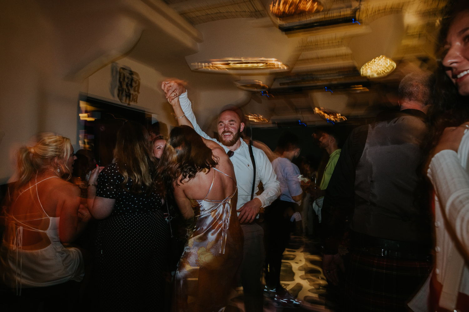 Mykonos wedding photographer: wedding guests dancing and spinning on the dance floor for Mykonos wedding celebration.