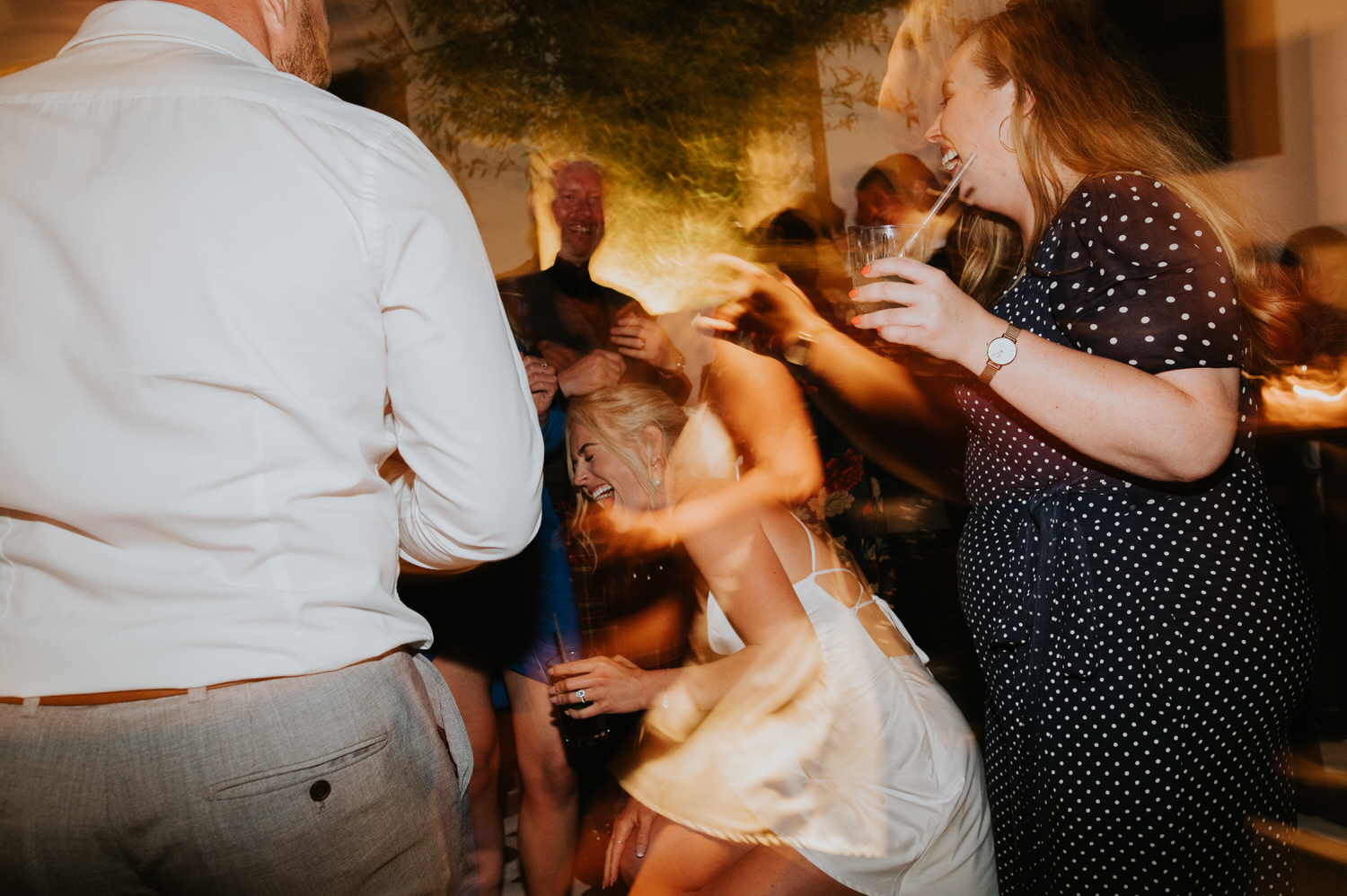 Mykonos wedding photographer: bride almost falls from the laughter on the dance floor among the guests.
