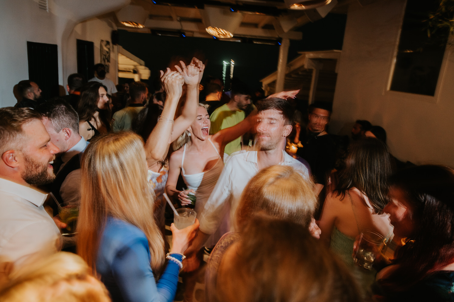 Mykonos wedding photographer: bride and guests screaming on the dance floor at Scarpa bar for her Mykonos wedding celebration.
