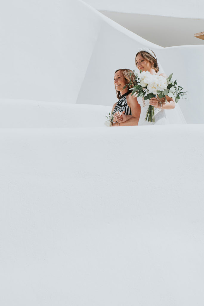 Rocabella Santorini Wedding: bride and mother photographed from ceremony terrace on the winding paths by Wedding photographer Santorini.